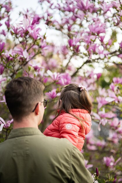 O irmão mais velho segura a irmã em seus braços enquanto desfruta de um belo dia de primavera perto da árvore de magnólia florescendo Atividades de primavera