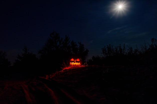 O jack-o-lantern de abóbora de halloween esculpido com velas acesas brilha na escuridão. Paisagem assustadora