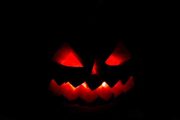 O jack-o-lantern de abóbora esculpido de halloween brilha na escuridão