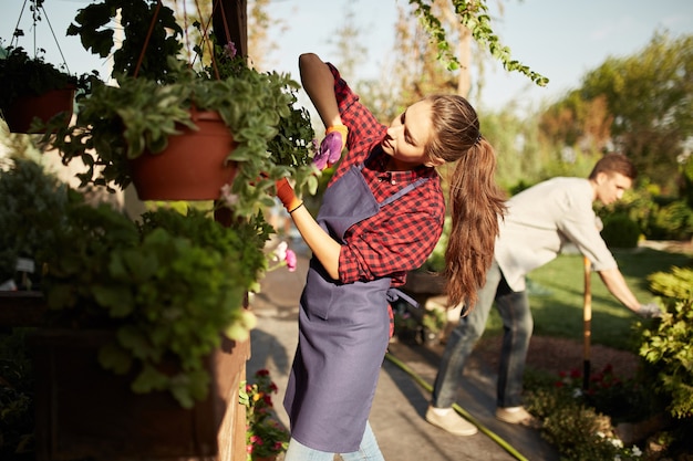 O jardineiro linda garota cuida das plantas no vaso na varanda enquanto o cara cava o solo com uma pá no maravilhoso jardim em um dia ensolarado.