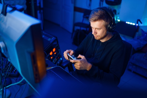 O jogador masculino com fones de ouvido segura o joystick e joga videogame no console ou PC de mesa, estilo de vida de jogo, ciberesporte. Jogador de jogos de computador em sua sala com luz de néon, streamer