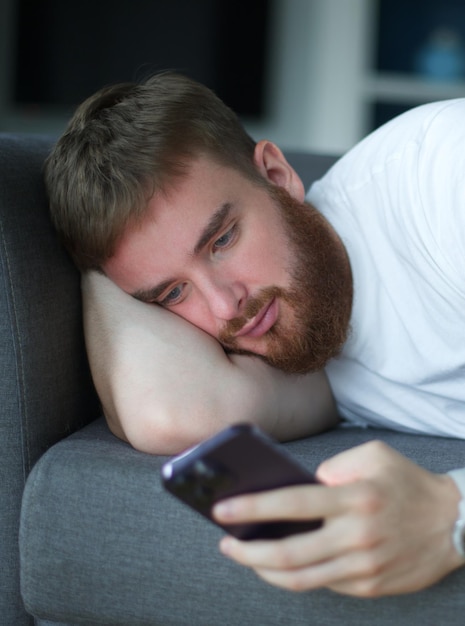 O jovem adulto relaxa chato no sofá usando smartphone para pessoas de lazer online, bem, descanse em