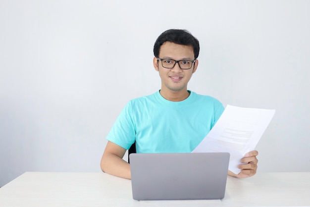 O jovem asiático está sorrindo e feliz ao trabalhar em um laptop e documentar o homem indonésio vestindo camisa azul