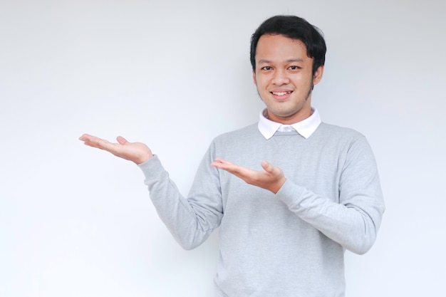 O jovem asiático está sorrindo e feliz com o ponto de mão no espaço vazio