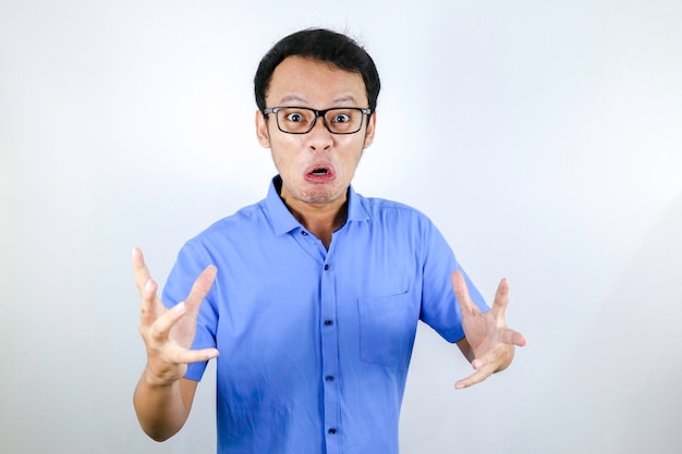 O jovem asiático usa camisa azul é um rosto engraçado com raiva com gritos e dedos apontando para a câmera isolada sobre fundo branco