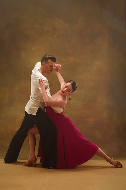 O jovem casal de dança de salão com vestido de ouro dançando em pose sensual no fundo do estúdio. Dançarinos profissionais dançando tango. Conceito de dança de salão. Emoções humanas - amor e paixão