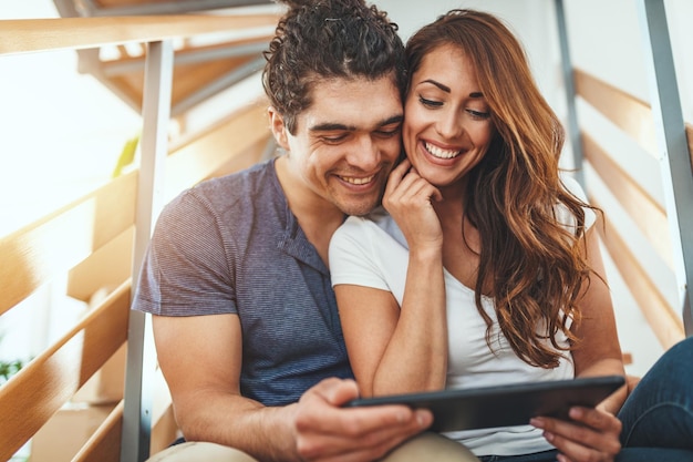 O jovem casal está se mudando para uma nova casa. Eles estão olhando para tablet digital e discutindo ideias de renovação.