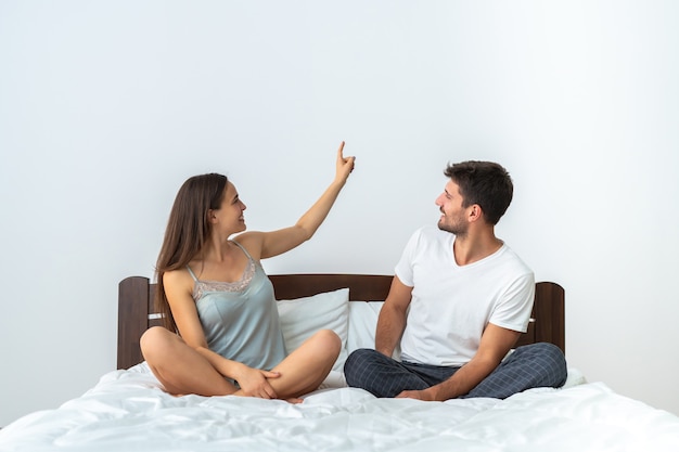 O jovem casal sentado na cama gesticulando no fundo branco