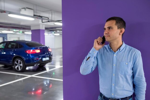 O jovem com telefone no estacionamento subterrâneo contra o fundo do carro