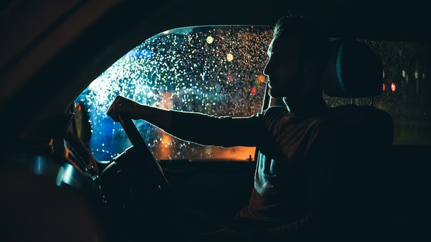 O jovem dirige o carro na estrada chuvosa à noite