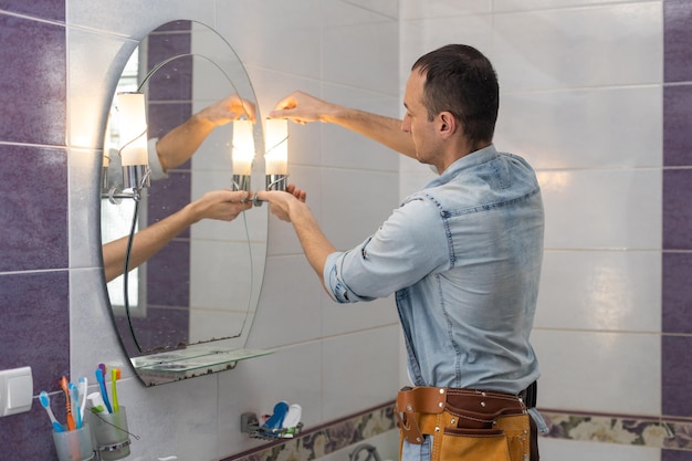 O jovem e bonito construtor está torcendo a lâmpada. O homem está olhando para cima.