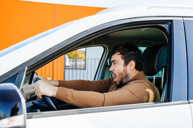 O jovem está segurando o volante e gritando no carro, ele tem uma expressão estranha no rosto