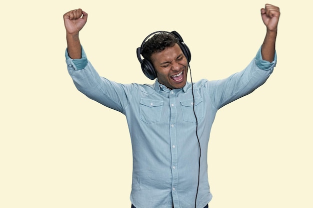 O jovem indiano emocional usa camisa azul para ouvir música em fones de ouvido isolados no fundo branco