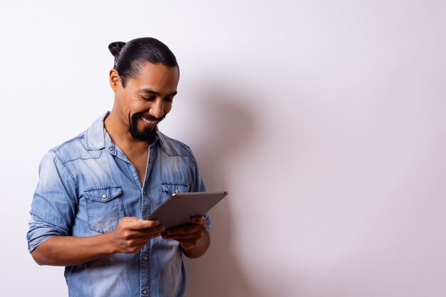 O jovem latino moderno e bem tratado com uma barba sorri contente olhando para seu tablet para fazer uma compra e está de lado ou três quartos e deixa um espaço à direita.