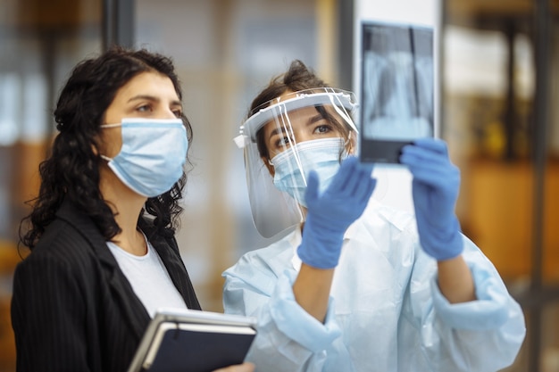 Foto o jovem médico mostra uma fotografia de raios-x dos pulmões ao paciente e explica o diagnóstico. prevenção e profilaxia de coronavírus. conceito de hospital e medicina.