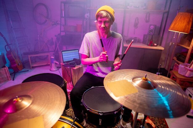 O jovem músico vai bater pratos com baquetas enquanto faz novas músicas durante o ensaio individual em sua garagem ou estúdio