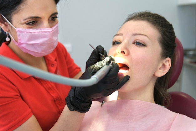 O jovem paciente feliz está sentado na cadeira do médico dentista na clínica odontológica e uma bela médica com máscara médica no rosto e luvas Visitando os dentes do dentista