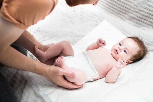 Foto o jovem pai troca a fralda de seu bebê. fundo branco. fechar-se. conceito de cuidados neonatais.