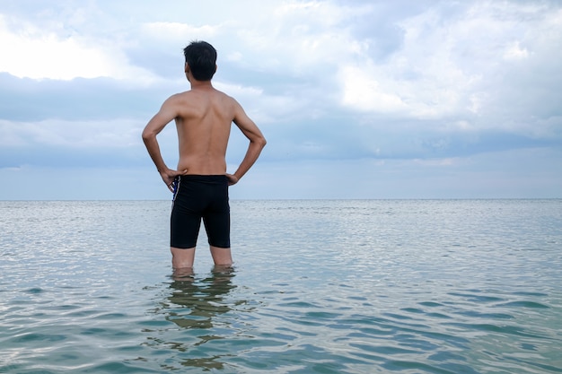 O jovem parado no mar deu as costas.