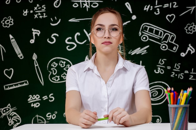 O jovem professor está sentado perto do quadro-negro na sala de aula.