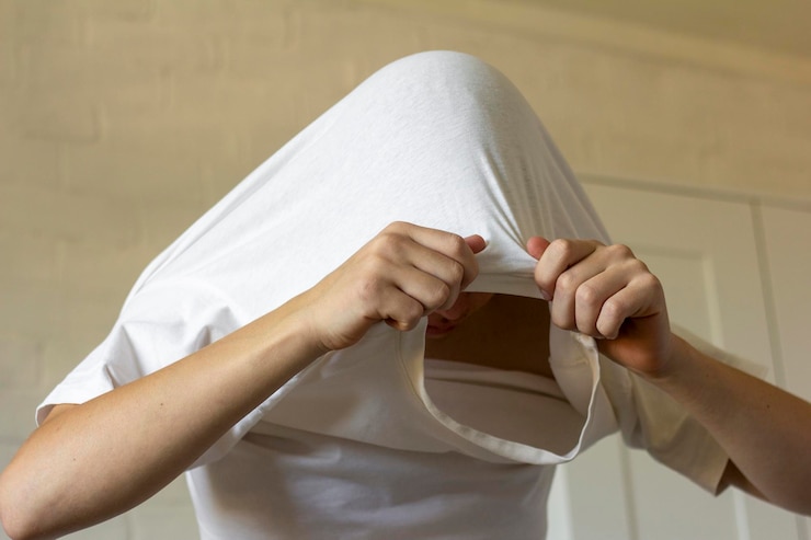 O jovem puxa a camiseta pela cabeça, tira a roupa.