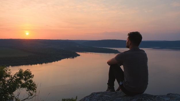 O jovem sentado na montanha rochosa acima do belo rio