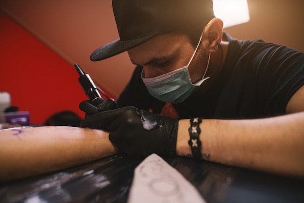 O jovem tatuador focado está pintando os braços dos clientes com cuidado em sua loja.