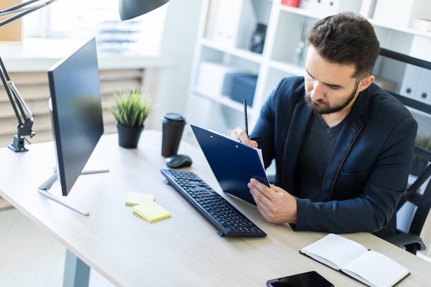 O jovem trabalha no escritório em uma mesa de computador com documentos, diagramas e telefone.