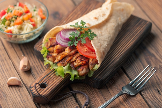 O kebab de Doner está encontrando-se na placa de estaca. Shawarma com carne de frango, cebola, salada encontra-se em uma mesa de madeira velha escura.