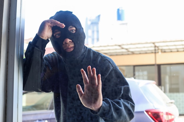 O ladrão em uma máscara preta olhando pela janela do apartamento