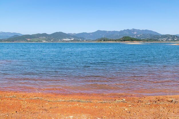 O lago sob o céu azul tem água azul e terra vermelha