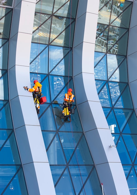 O limpador de janelas trabalhando em um arranha-céu moderno de fachada de vidro