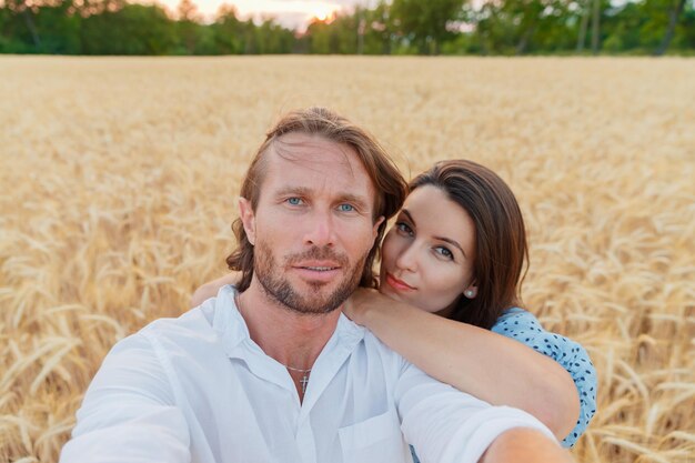 O lindo casal abraça no campo de trigo ao pôr do sol, eles estão felizes com os cabelos longos e fáceis