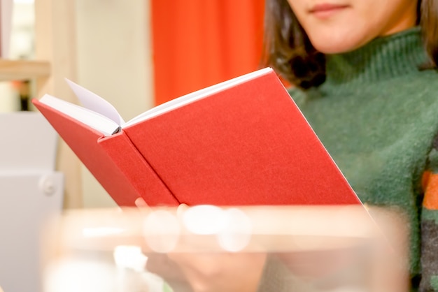 O livro vermelho aberto está segurando / lendo na mão de mulheres em casa