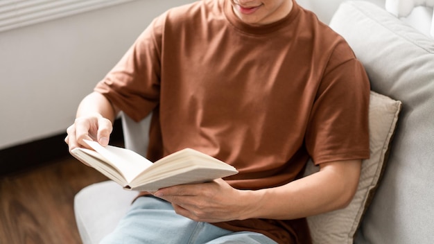 O macho com seus óculos sentado no sofá cinza inclinando as costas e lendo um livro