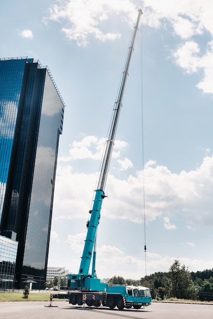 O maior e mais alto guindaste de carro azul está colocado em uma plataforma ao lado de um grande edifício moderno. O maior caminhão guindaste para tarefas complexas.