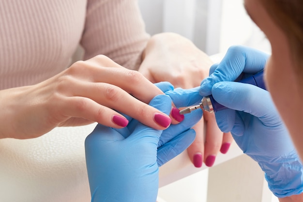 O manicure master usa uma máquina de unhas elétrica para remover esmalte das mãos no salão de beleza