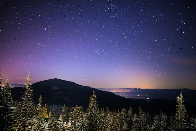 O maravilhoso céu estrelado está localizado acima das vistas pitorescas da estância de esqui entre as montanhas de colinas e árvores. conceito de férias de inverno. lugar para texto