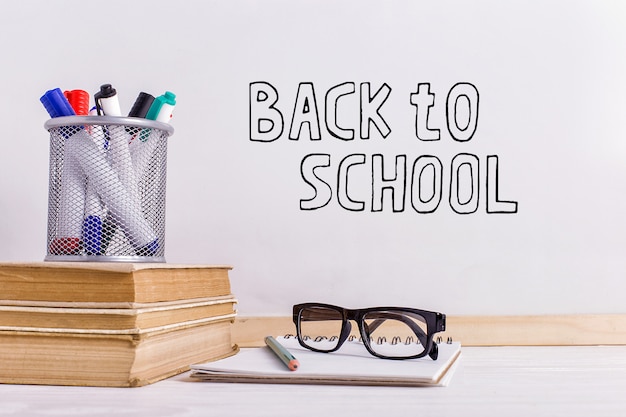 O marcador de inscrição em um quadro branco, back to school uma mesa com atributos de livros e óculos para escrever.