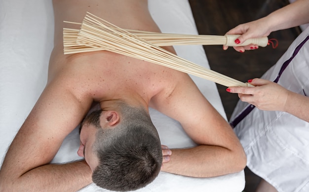 O massagista faz uma massagem japonesa em um homem com vassouras de bambu.