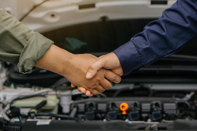 Foto o mecânico apertando a mão do cliente depois de terminar de verificar o serviço de reparação do sistema do carro