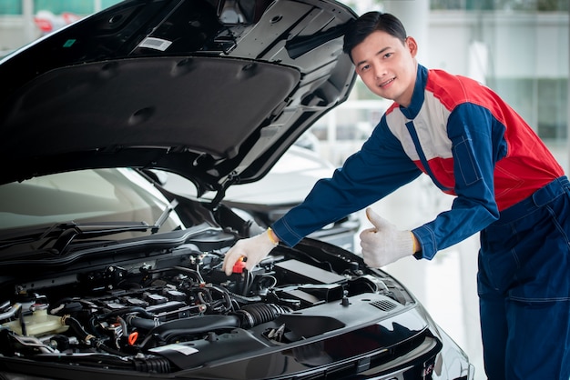 O mecânico de automóveis asiático em uma oficina de automóveis está verificando o motor. Para os clientes que usam carros para serviços de reparo, o mecânico trabalha na garagem.