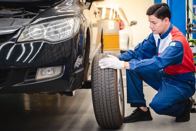 O mecânico de automóveis asiático está removendo a roda e verificando os freios e a suspensão no serviço de carro com uma empilhadeira. Centro de reparo e manutenção