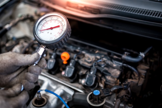 O mecânico de automóveis está prestes a medir a compressão no cilindro de um motor de carro usando um barômetro de diagnóstico e reparado na sala de máquinas de um veículo.