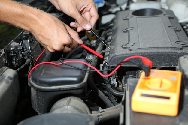 Foto o mecânico de automóveis usa um voltímetro multimetro para verificar o nível de tensão na bateria do carro