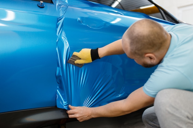 O mecânico instala uma película protetora de vinil ou filme na porta do veículo. Trabalhador faz detalhamento de automóveis. Proteção de pintura automotiva, ajuste profissional