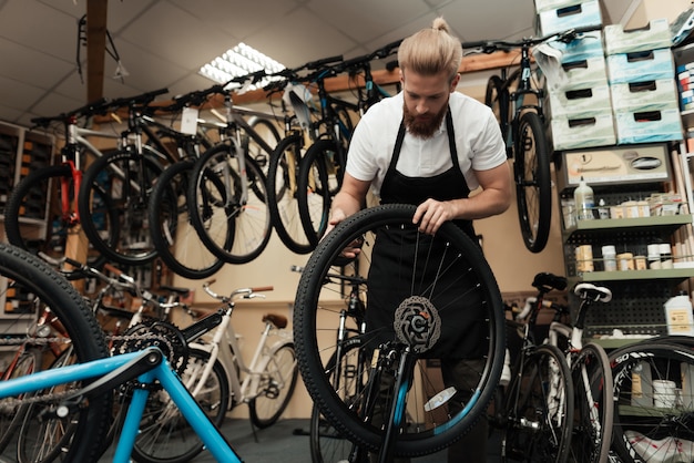 O mecânico novo repara a bicicleta na oficina da bicicleta.