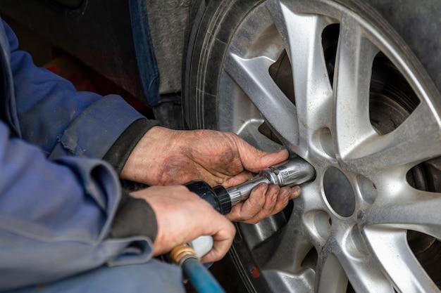 O mecânico sem luvas está trocando a roda do carro com uma chave pneumática