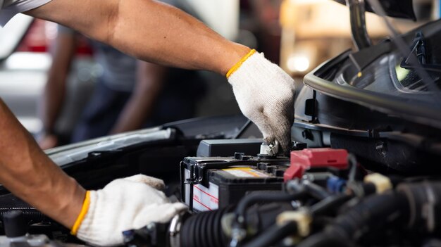 O mecânico sênior asiático de mão fechada usa voltímetro multímetro para verificar o nível de tensão na bateria do carro no serviço de carro e na garagem de manutenção