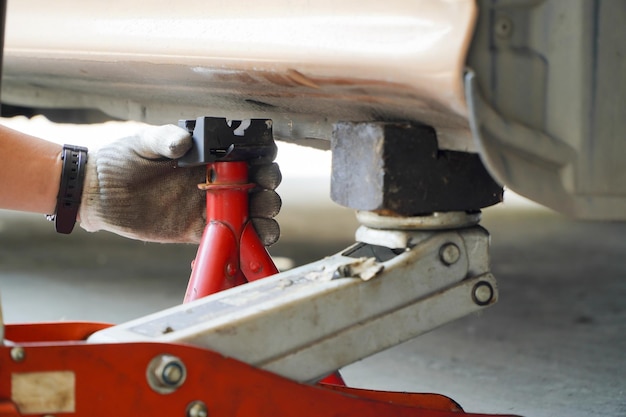 O mecânico usa o macaco para levantar o carro para consertar a suspensão do carro Mudança de pneu sazonal ou conceito abstrato de serviço